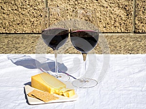 2 glasses of wine with cheddar cheese, and crackers on an outdoor table