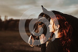 2 heads one love! stallion with head collar and redhead woman are bonding while being intimate friends and look left into sun to