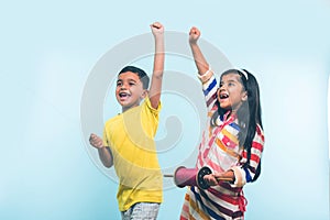 2 indian kids flying kite, one holding spindal or chakri