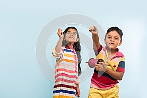 2 indian kids flying kite, one holding spindal or chakri