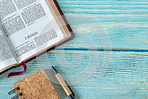 2 Kings open Holy Bible Book with a notebook and pen on a wooden background with copy space