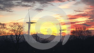 2 large wind turbines turning in a field next to lake with deep orange sunset sky. south wales uk pen y fan pond. clean