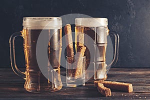 2 mugs of light beer with croutons on a dark wooden background, alcoholic drink