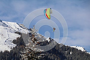 2 people paragliding in a tandem flight with a sunny winterlandscape with snow covered mountains in the background