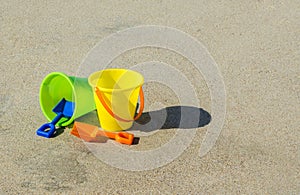 2 plastic sand pails and shovels on a smooth sandy beach