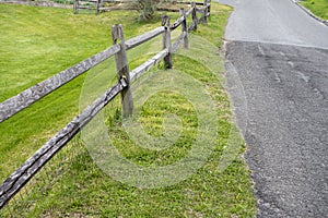 2 Rail Post wood fence along a blacktop road with green grass lawn