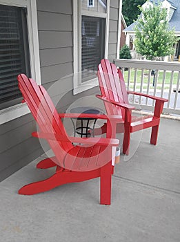 2 red Adirondack style chairs on a front porch
