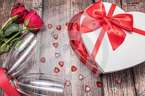 2 red roses with champagne flutes and a heart shaped gift box.