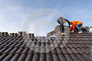 2 Roofers worker in protective uniform wear and gloves, using air or pneumatic nail gun and installing Concrete Roof Tiles on top
