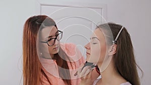 2 shots. Professional make-up artist applying powder to woman face