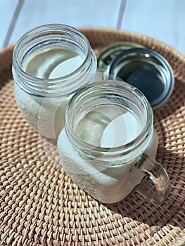2 Two glasses of mason jars with natural homemade plain yoghurt, yogurt, on the handwoven rattan tray, wicker basket,