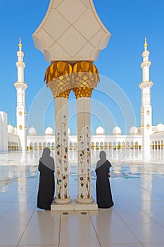 2 (two) tourist women wearing traditional black Abaya clothing admiring the beauty of Sheikh Zayed Grand Mosque in Abu