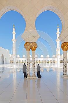 2 (two) tourist women wearing traditional black Abaya clothing admiring the beauty of Sheikh Zayed Grand Mosque in Abu