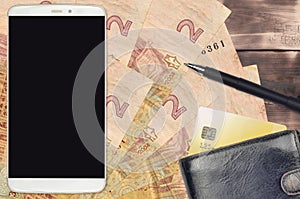 2 Ukrainian hryvnias bills and smartphone with purse and credit card. E-payments or e-commerce concept. Online shopping and