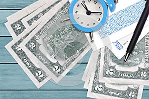2 US dollars bills and alarm clock with pen and envelopes. Tax season concept, payment deadline for credit or loan. Financial
