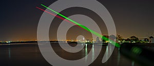 2 visible beams of laser light, red and green, focusing in the direction of Lisbon, crossing the Tagus River