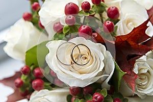 2 wedding rings lie on a bouquet of white roses, flowers