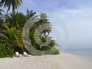 2 white beach chairs on sand beach of tropical island