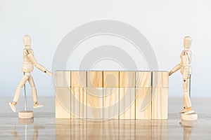 2 wooden puppets building a wooden wall on a table, white background, protection concept.