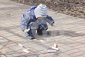 A 2 -year-old boy painting with chalk outdoors