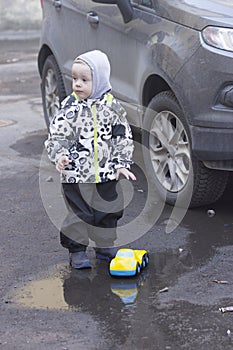 A 2 -year-old boy playing with a toy car in a puddle near a real car