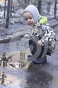 A 2 -year-old boy playing with a wooden stick in a puddle