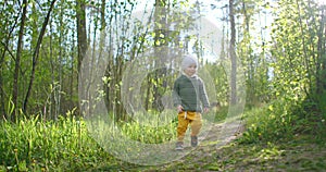 A 2-year-old Caucasian boy walks in slow motion along forest paths in a pine forest. Walks in the Park. Adventures of a