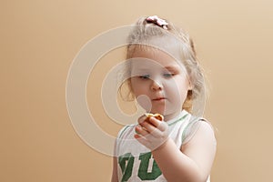 A 2-year-old girl stands on a beige background and holds a cookie in her hand. Happiness is motherhood. Lovely