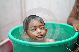 2-year-old Indian baby boy enjoying a bath in a green tub.
