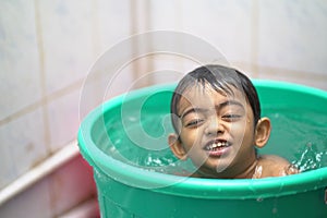 2-year-old Indian baby boy enjoying a bath in a green tub.