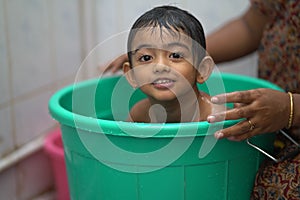 2-year-old Indian baby boy enjoying a bath in a green tub.