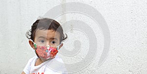 2-year-old Latin girl with protective mask on white wall background, new normal covid-19