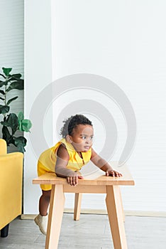 A 2-year-old Nigerian baby girl with beautiful curly hair, climbing a table with a mischievous