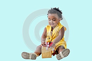 A 2-year-old Nigerian baby girl with beautiful curly hair, smiling and happy with gift box