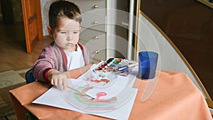 A 2 years old child draws a rainbow with paints. Creative activities at home concept. Children's desk, drawing supplies