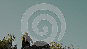 20`s One man raising his arms up after climbing on a rock with a yellow coat and a backpack