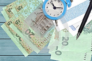 20 Ukrainian hryvnias bills and alarm clock with pen and envelopes. Tax season concept, payment deadline for credit or loan.