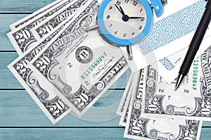 20 US dollars bills and alarm clock with pen and envelopes. Tax season concept, payment deadline for credit or loan. Financial