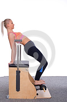 A 20-year-old trainer practices Pilates on an elevator chair, bending into a bridge position.