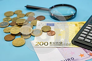 200 Euro banknote, coins, calculator and magnifier on a blue background. Finance concept.
