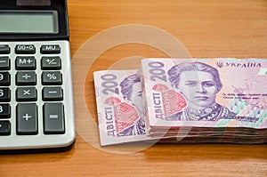 200 hryvnia and a calculator on a wooden table. Close-up.