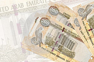 200 UAE dirhams bills lies in stack on background of big semi-transparent banknote. Abstract presentation of national currency