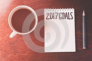 2017 goals list with notebook, cup of coffee on wooden table.