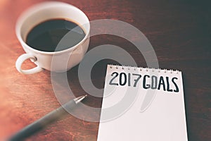 2017 goals list with notebook, cup of coffee on wooden table.