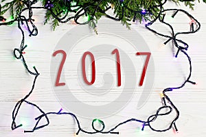 2017 sign text on christmas frame of garland lights on fir branches. stylish border on white rustic wooden background. space for