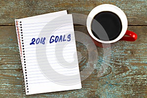 2018 goals list with notebook, cup of coffee on wooden desk. To