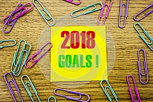 2018 goals on yellow sticky note, on wooden background. New Year resolutions concept.