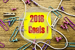 2018 goals on yellow sticky note, on wooden background. New Year resolutions concept.