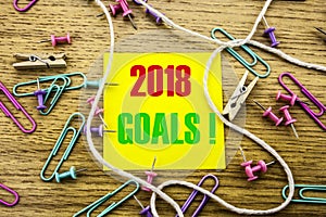 2018 goals on yellow sticky note, on wooden background. New Year resolutions concept.