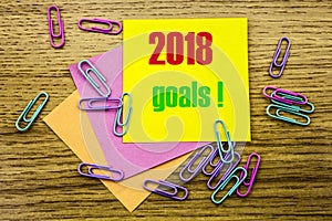 2018 goals on yellow sticky note, on wooden background. New Year resolutions concept.